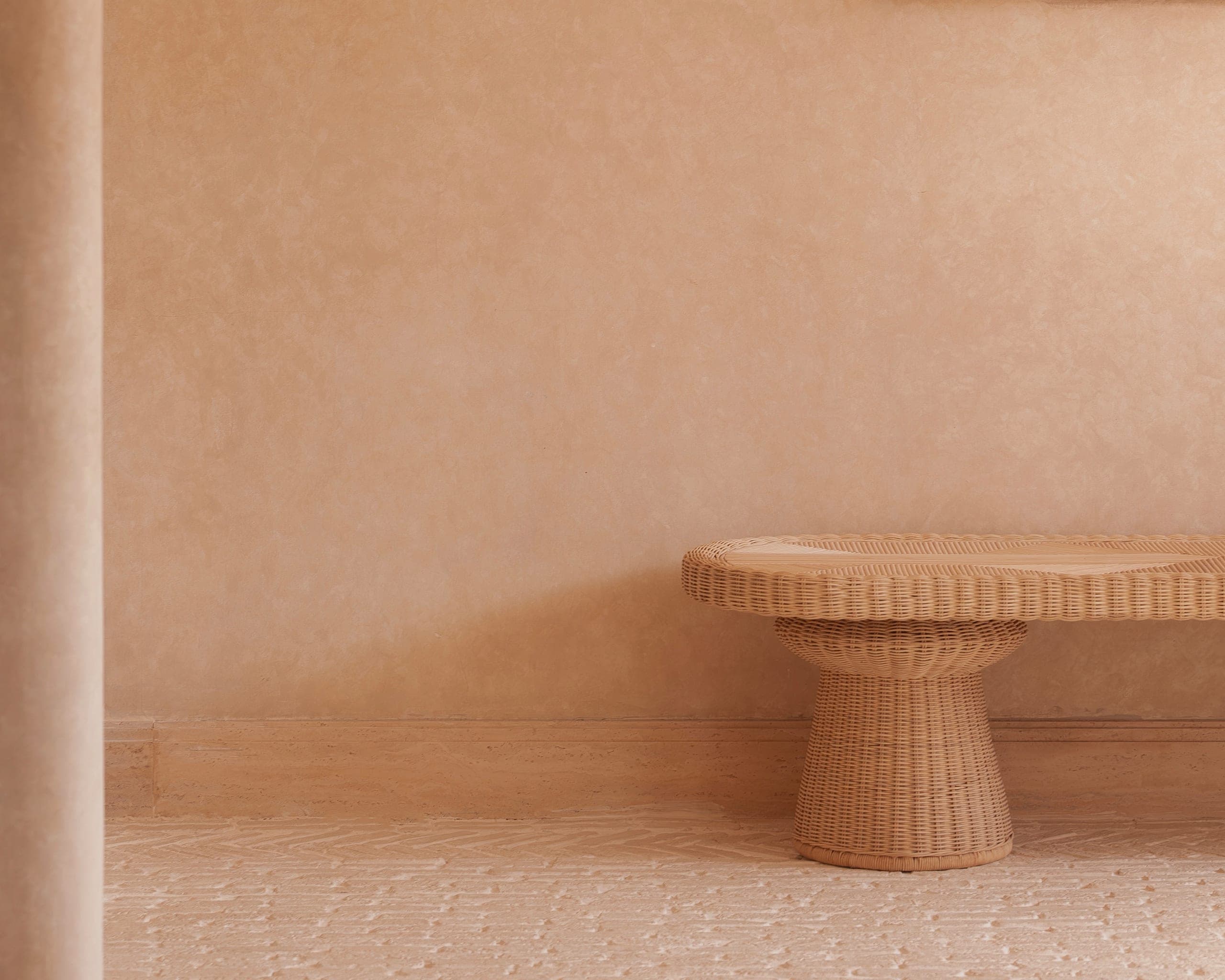 A quiet studio interior, a rattan bench against a sand-coloured plaster wall